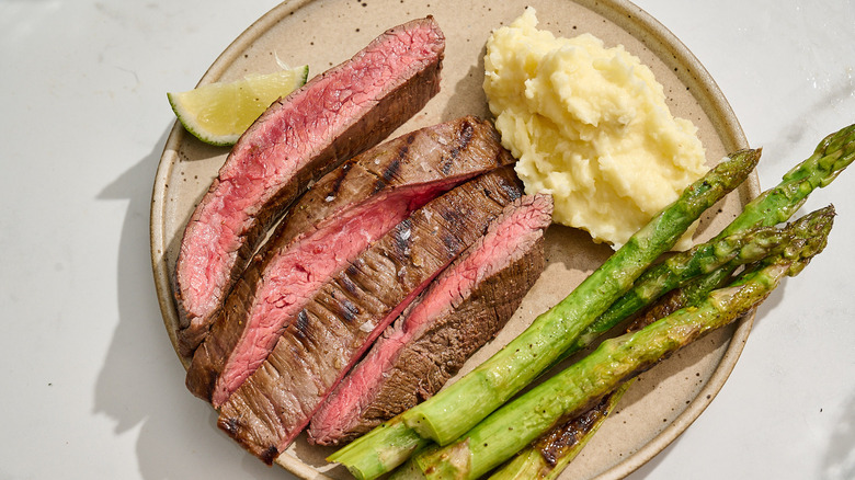 slices of flank steak on a plate with mashed potatoes and asparagus