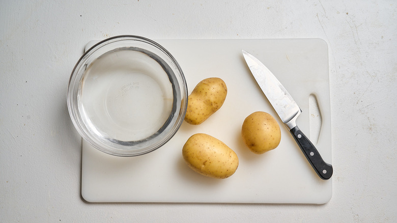 bowl of water on a cutting board with potatoes