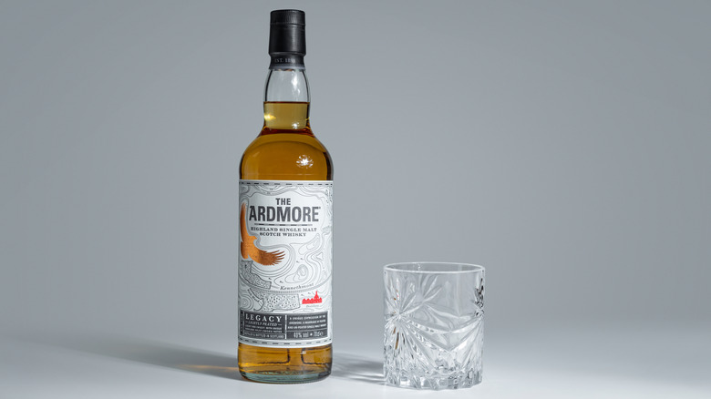 Bottle of The Ardmore Legacy next to a glass on a plain background
