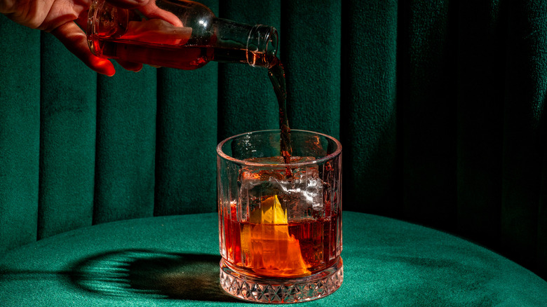 Hand pouring bottle of vermouth into glass