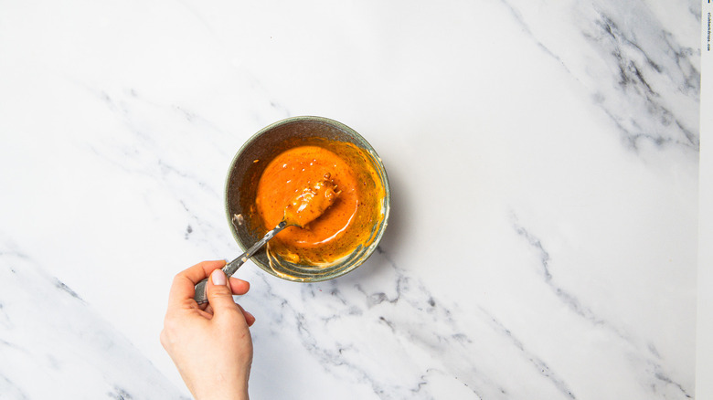 Mixing spicy sauce in a bowl with fork.
