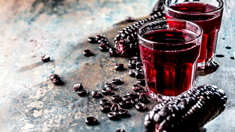 Two glasses of chicha morada surrounded by purple corn kernels
