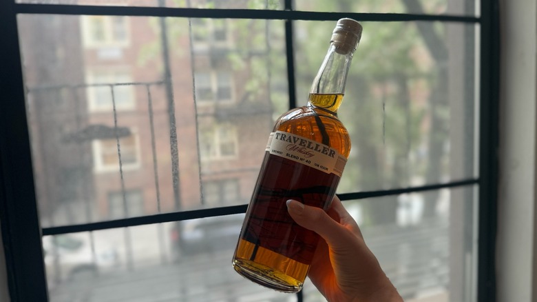 bottle of Traveller Whiskey being held up in front of a window