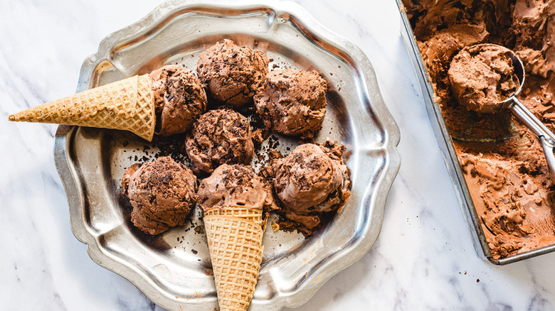 Scoops of chocolate ice cream in metal dish and in waffle cones
