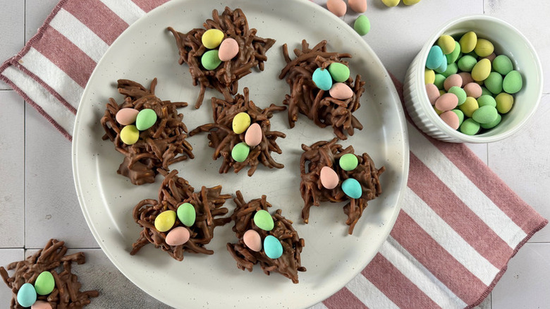 Easter-themed bird's nest cookies on plate next to bowl of mini eggs