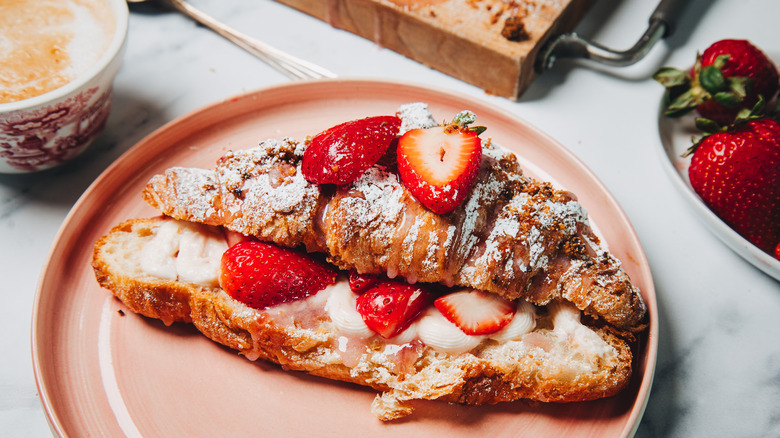 Strawberry cheesecake croissant on a pink plate beside a coffee.