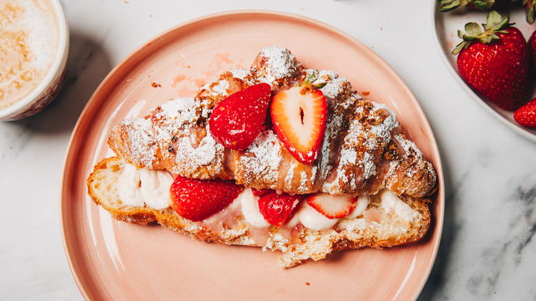 Strawberry cheesecake croissant on a pink plate besides a coffee.