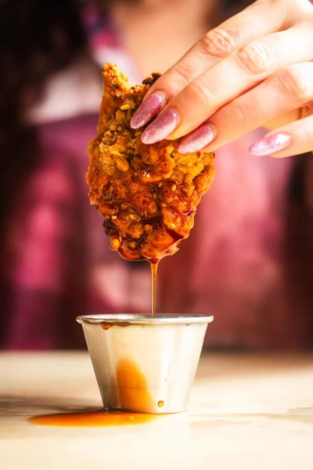 Close up of fried chicken being dipped in sauce