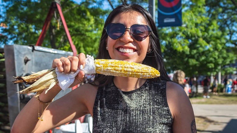 A person at Summerfest posing with a large corn