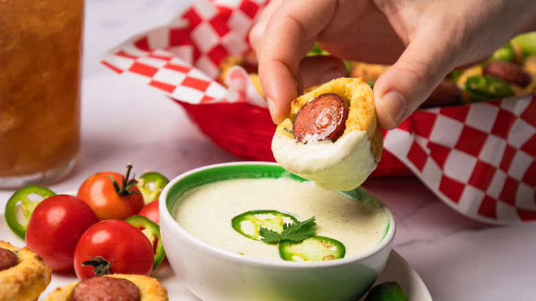 Close up on dipping a corn dog into spicy jalapeño crema.
