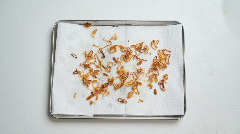 draining fried onions on a paper towel lined sheet tray