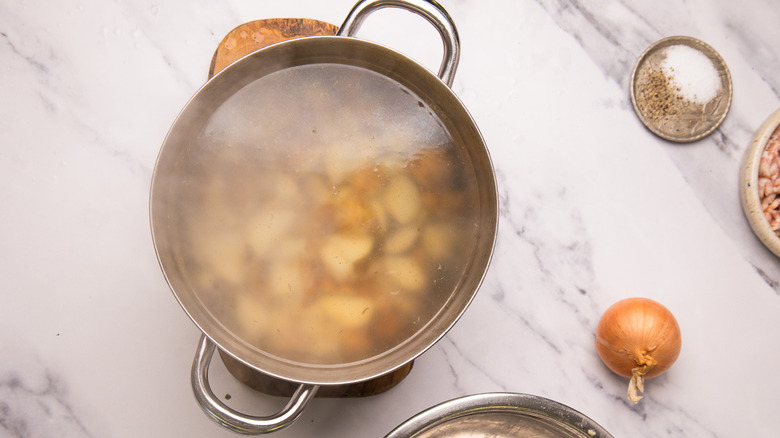 Boiling potatoes in pot with salt, pepper and onions around.