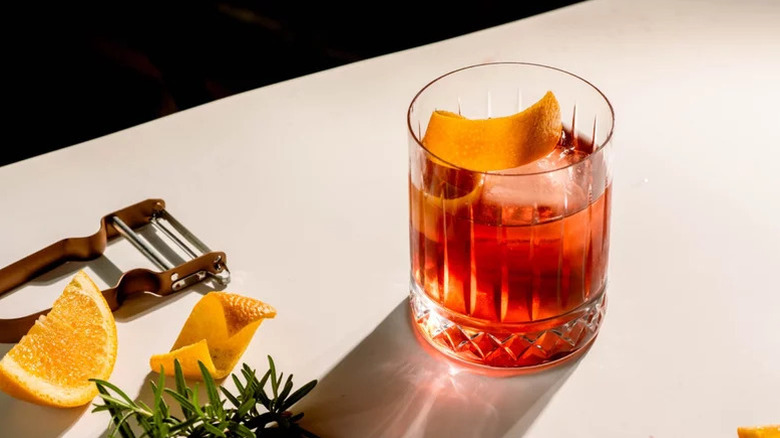 Negroni cocktail in an old-fashioned glass on a white table next to bar tools and garnishes.