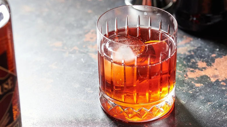 A boulevardier cocktail in an old-fashioned glass on a black bartop.