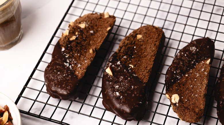 Three chocolate biscotti on a rack with coffee in background.