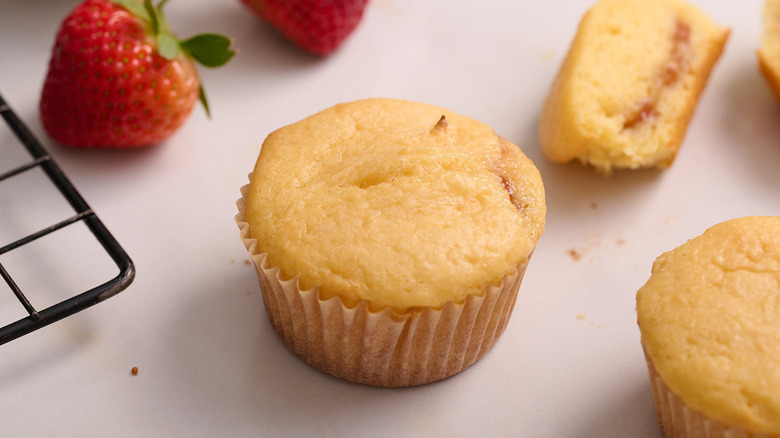 Strawberry muffins next to fresh strawberries and wire cooling rack