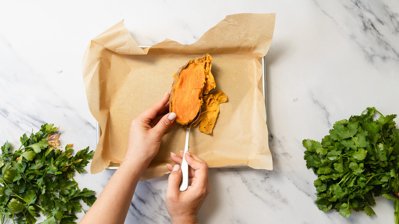 Spoon removing sweet potato flesh on baking sheet