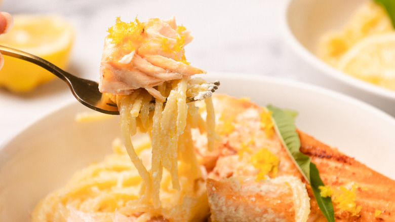 Lifting a forkful of flaked salmon over a bowl of creamy citrusy salmon pasta.