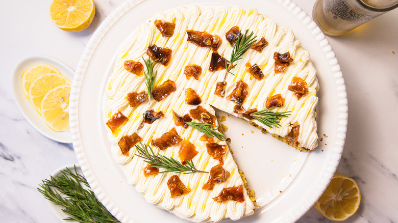 Gluten-free lemon olive oil cake with slice taken out, and rosemary, lemon and olive oil around it.