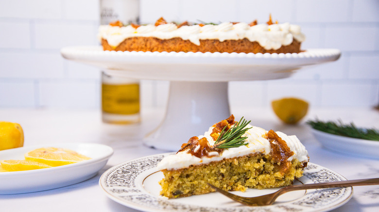 Gluten-free lemon olive oil cake with slice taken out, and rosemary, lemon and olive oil around it.