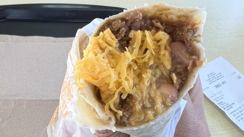 A Del Taco burrito packed with extra cheese held in someone's hand