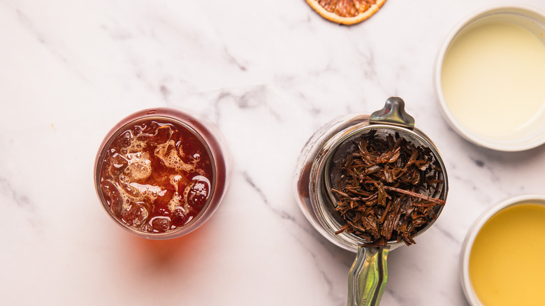 Glass of tea and ice next to tea leaves in strainer