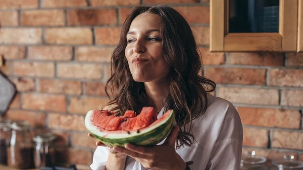 Woman at home eating watermelon in the kitchen.