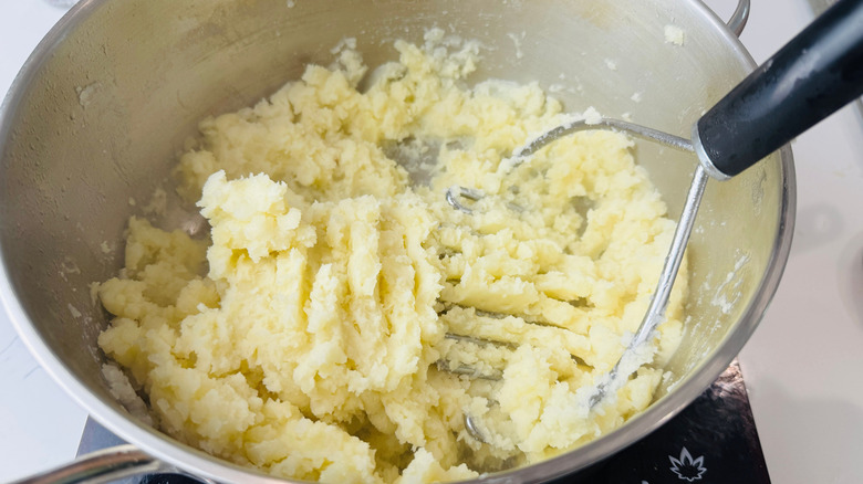 Mashing potatoes with potato masher in pot