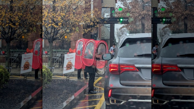 a Chick-fil-A employee taking drive-thru orders in the rain while wearing a strange rectangular covering