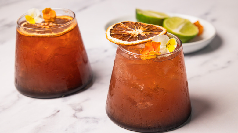 Two blood orange rum sunset cocktails with garnishes in background