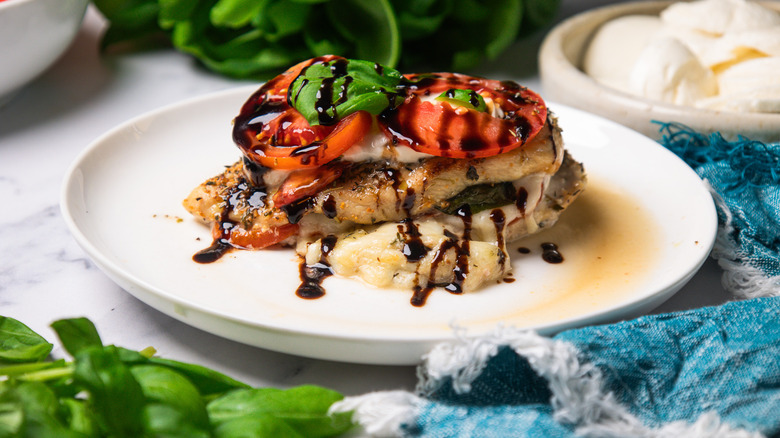 A Caprese-stuffed chicken breast on a white plate next to basil