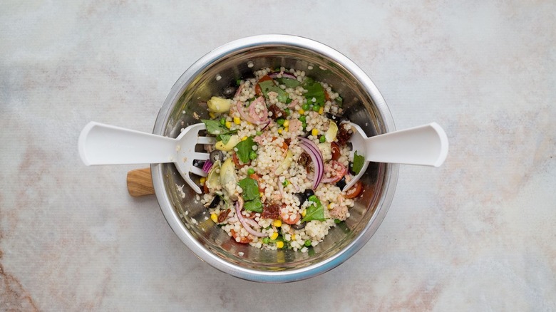Mixed tuna couscous salad in bowl with mixing utensils