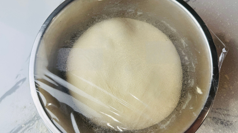 Dough in bowl covered with plastic wrap