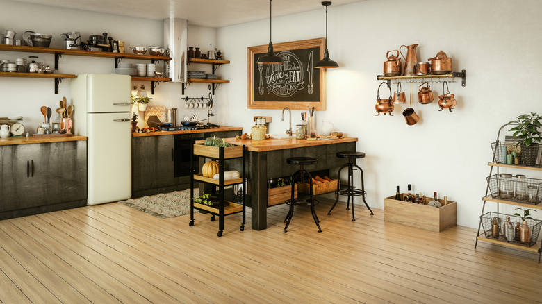 A compact kitchen in a corner of a larger open-floor-plan space, with open shelving where the upper cupboards would normally be