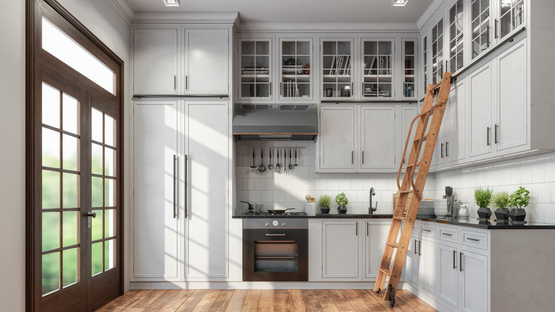 A sleek, modern kitchen, with double-height cabinets in white and glass, with a library-style rolling ladder for access to the highest level
