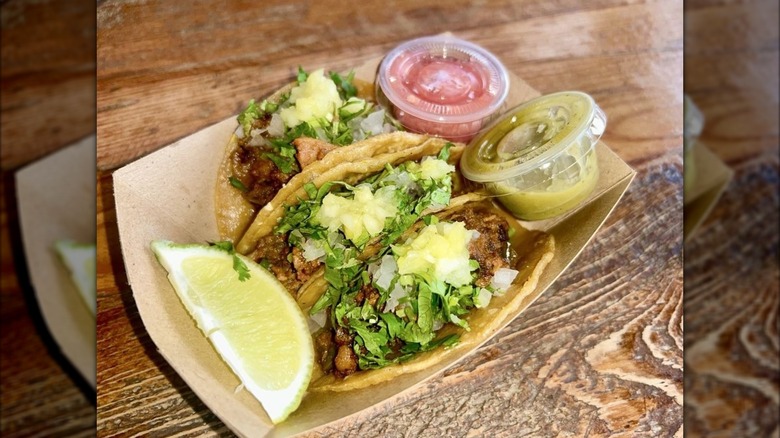 Three meat tacos in tray served with herbs