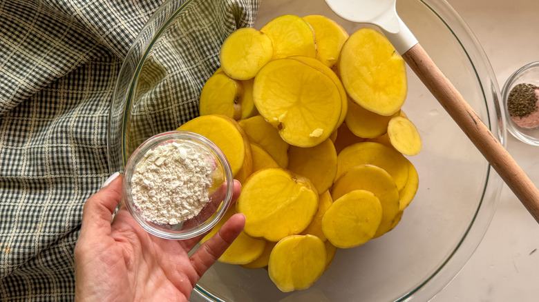 hand adding flour to bowl with potato slices