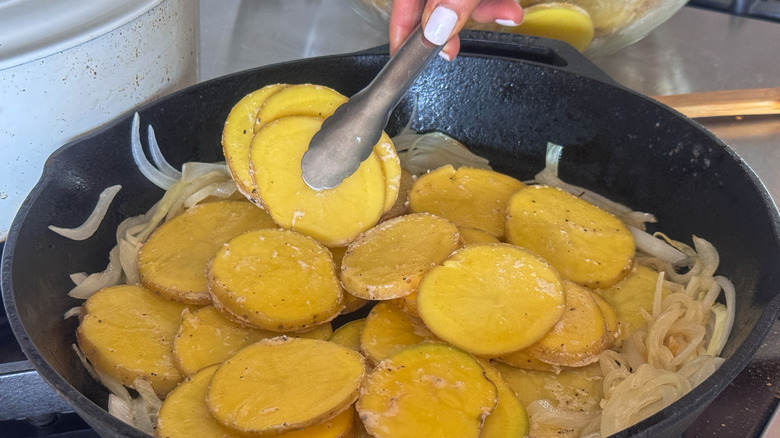 tongs placing potato slices in skillet