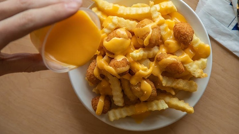 Pouring cheese sauce on fries and curds