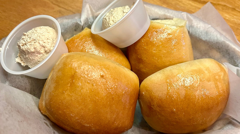 Four Texas Roadhouse rolls in a basket with cups of butter