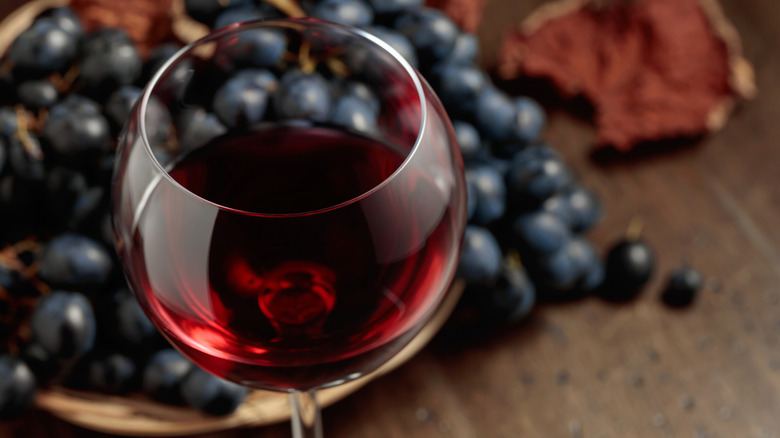 Glass of merlot in front of a bunch of black grapes