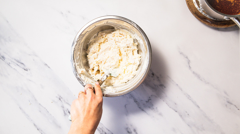 Hand stirring spatula inside bowl of Nashville hot chicken dip