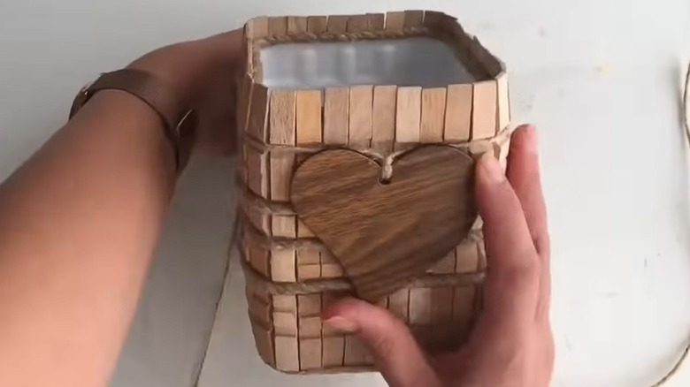 Hands holding wooden canister made from old milk jug and clothes pins