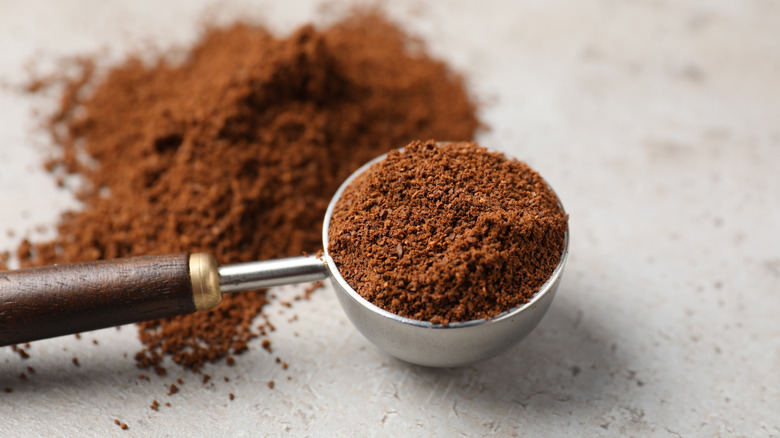 Scoop of freshly ground coffee next to pile