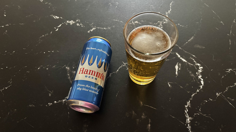 Hamm's beer can next to a glass of beer on a dark counter
