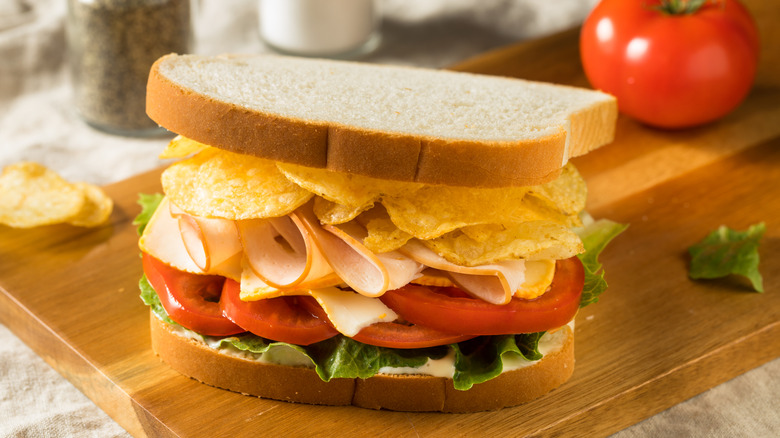 Sandwich with potato chips and tomatoes inside on a cutting board