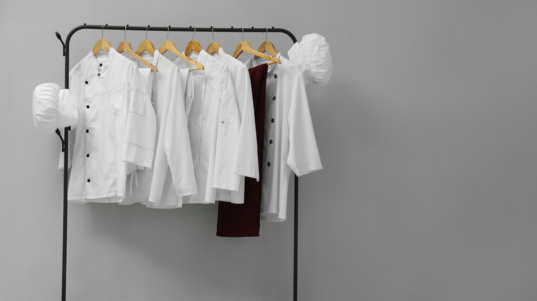 A selection of chef hats and jackets hang on a clothing rack.