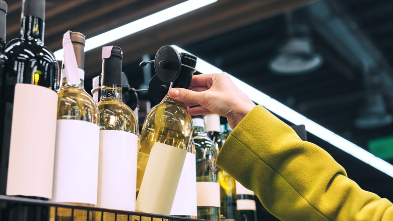 hand reaching for white wine bottle on shelf