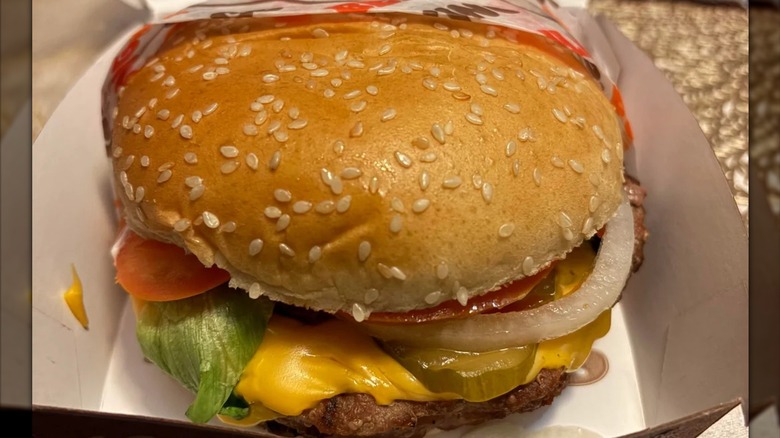 A Burger King Burger on a sesame seed bun with visible cheese, pickle, lettuce, tomato, and onion in a box