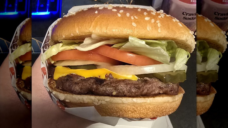 A close-up of a New Whopper in its wrapper, being held in a person's hand